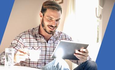 Bearded man sips tea while using Bill Pay to pay his bills on a tablet
