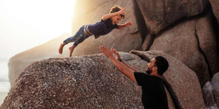 child jumping off a rock into the arms of an adult man