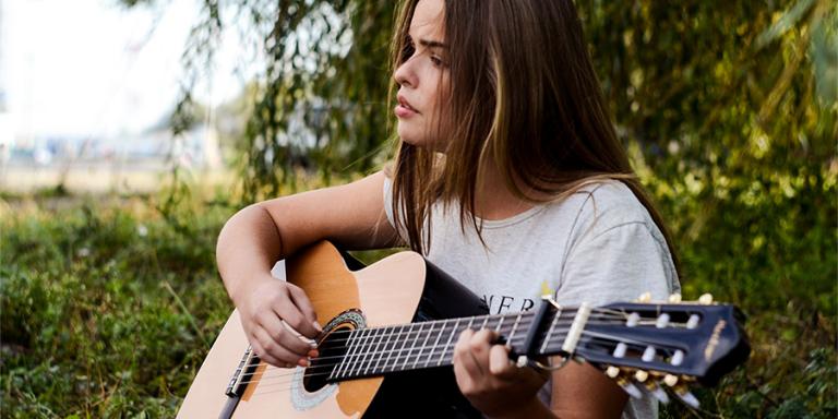 A young woman plays guitar in the woods