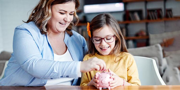 A mother puts a coin in her daughter's piggy bank. 