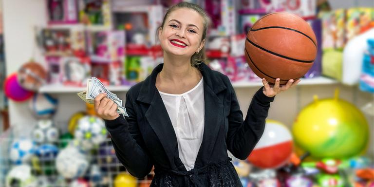 A young girl smiles at the camera holding a basketball and dollar bills