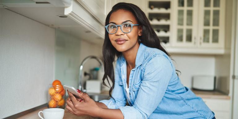 Smiling woman leaning on counter holding her phone.