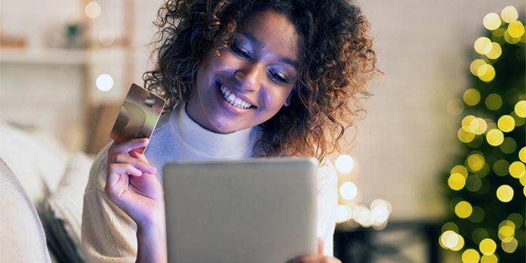 Woman smiles as she holds her credit card in front of her tablet screeen