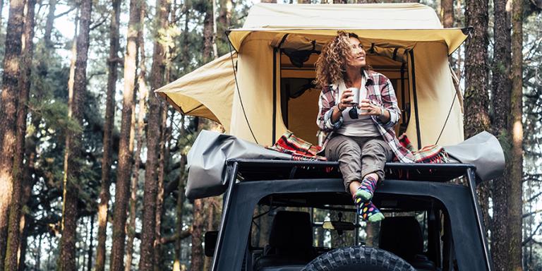Woman sitting on jeep in woods