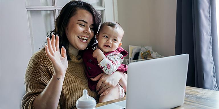 Mother and baby sitting at table and looking at a laptop