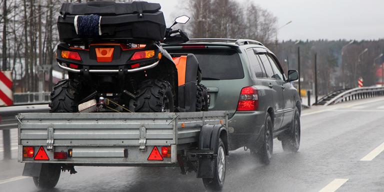 Car hauling a trailer with an ATV on it.