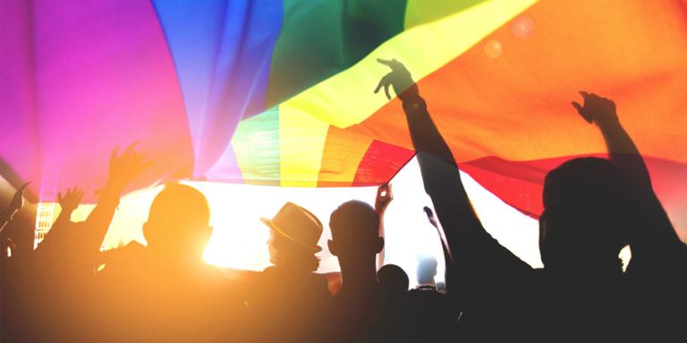 Rainbow flag with people under it at a celebration