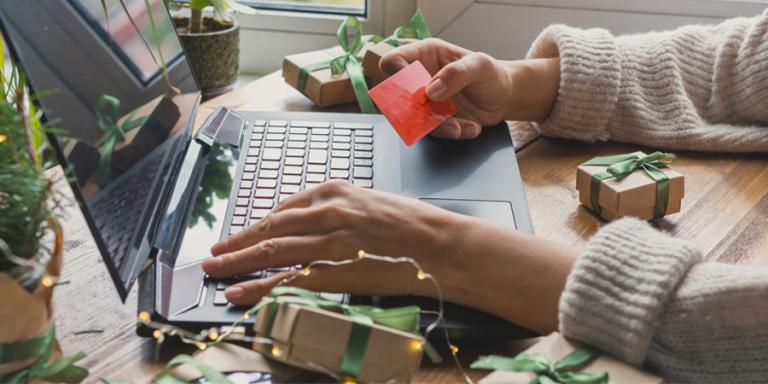 Laptop surrounded by gifts with hands typing on the keyboard