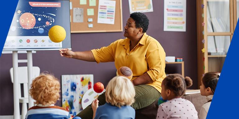 Teacher in a classroom showing young children a model of the solar system.