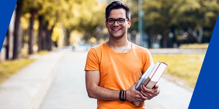 College student holding his textbook and smiling at camera.