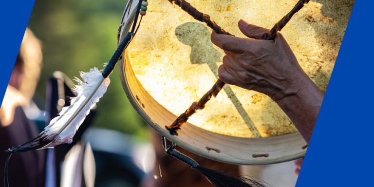 A traditionally constructed native drum is seen in the hands of a indigenous person celebrating traditional music.