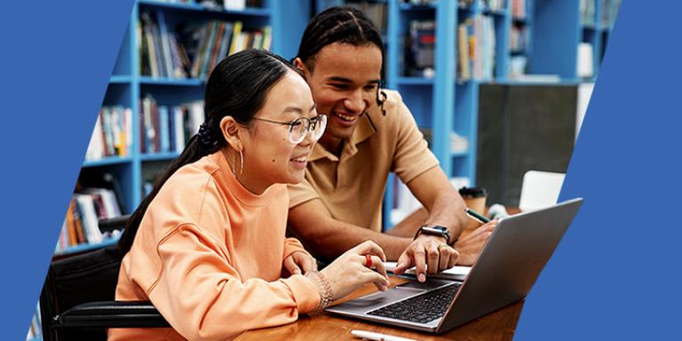 Two students sitting at desk with laptop in library