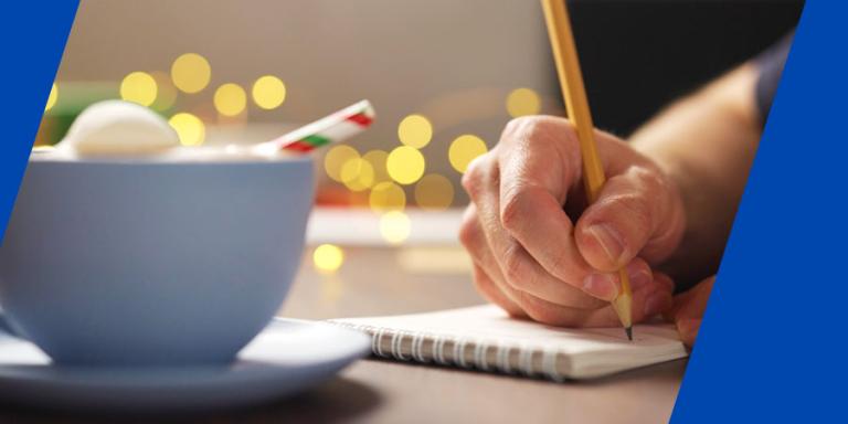 Person making a shopping list and drinking hot cocoa.