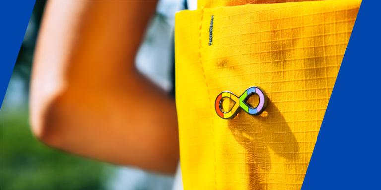 Autism rainbow infinity loop pin on a bright yellow backpack.