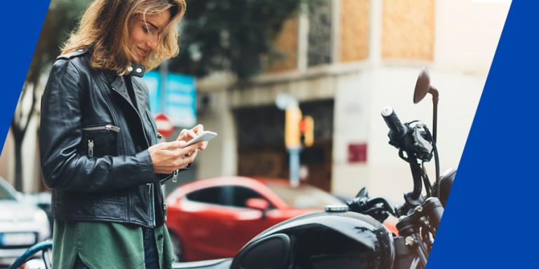 Woman checking her phone before gearing up to ride her motorcycle.
