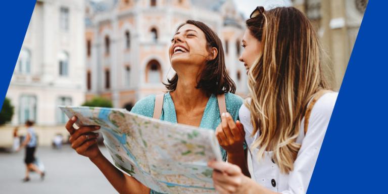Two female friends looking at a map traveling in an European city.