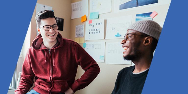 Two smiling students hanging out in a college dorm.