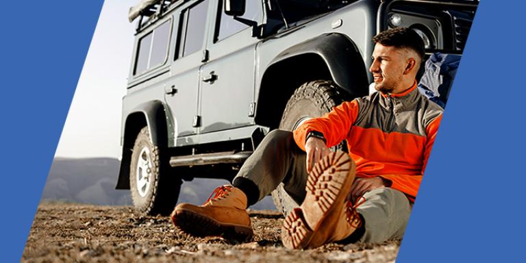 Hiker resting in front of 4 wheel drive vehicle.