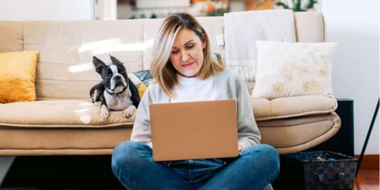 A women using her laptop while a little dog watches