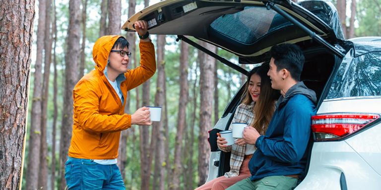 Friends having a cup of coffee while sitting on the tailgate of their SUV
